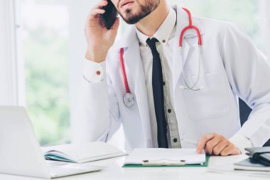 Doktor hastanede ofis masasında cep telefonu üzerinde konuşurken. Tıbbi ve sağlık kavramı.
