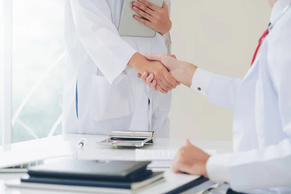 Doctor at the hospital giving handshake to another doctor showing success and teamwork of professional healthcare staff.