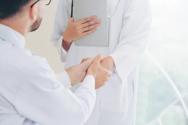 Doctor at the hospital giving handshake to another doctor showing success and teamwork of professional healthcare staff.