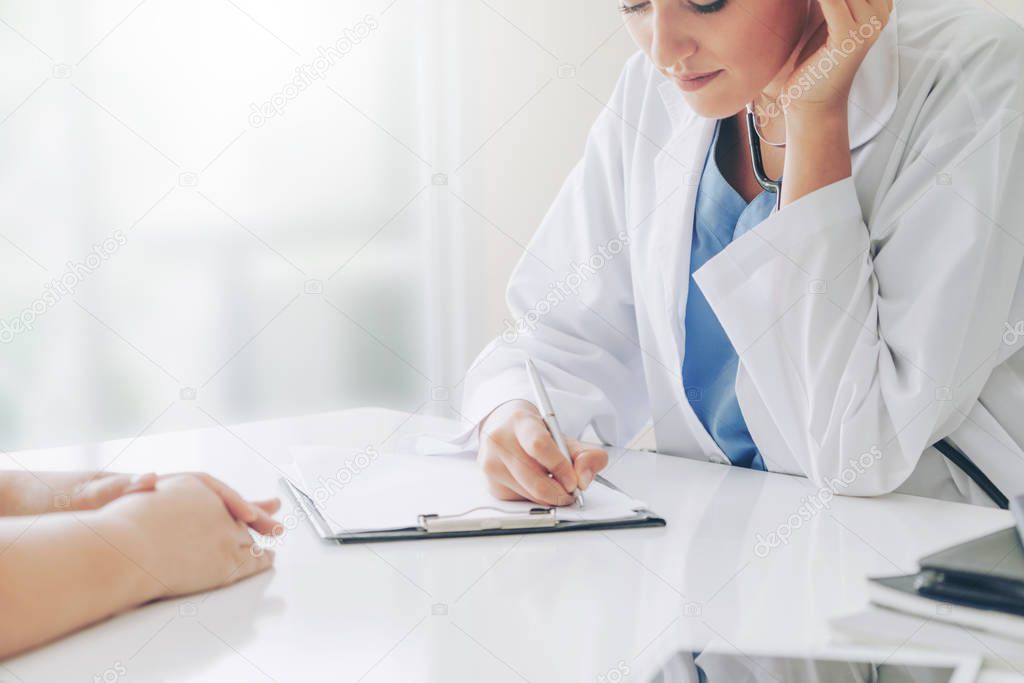 Woman doctor talks to female patient while writing on the patient health record in hospital office. Healthcare and medical service.