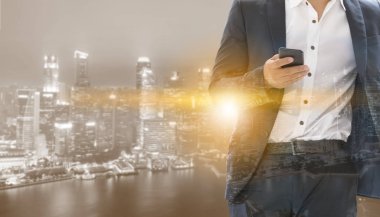 Genç işadamı cep telefonunuzun ve modern şehir binaları arka plan ile. Gelecekteki telekomünikasyon teknolojisi ve internet şeyler (çok) kavramının.