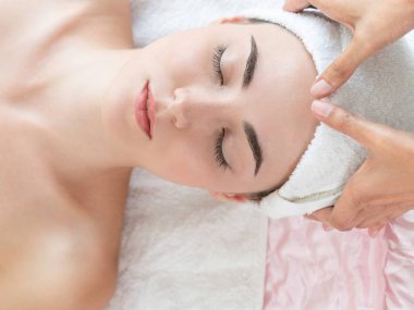 Lüks bir spa merkezinde masaj terapisti tarafından yüz masajı ve spa tedavisi için kaplıcaya uzanmış rahat bir kadın. Sağlık, stres atma ve gençleştirme kavramı.