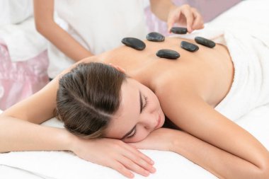 Kadın kaplıca salonunda profesyonel güzellik terapisti tarafından sıcak taş masajı görüyor. Lüks sağlık, sırt stresi ve gençleştirme kavramı..