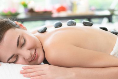 Kadın kaplıca salonunda profesyonel güzellik terapisti tarafından sıcak taş masajı görüyor. Lüks sağlık, sırt stresi ve gençleştirme kavramı..