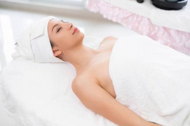 Spa yatağında uzanan rahat genç bir kadın lüks bir spa merkezinde yüz bakımı ve masaj için hazırlandı. Sağlık, stres atma ve gençleştirme kavramı.