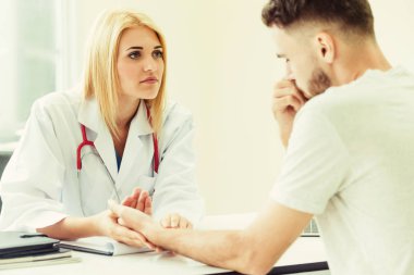 Kadın doktor konuşuyor ve erkek hasta hastane ofisinde inceleyerek. Sağlık ve tıbbi hizmet.