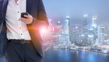 Genç işadamı cep telefonunuzun ve modern şehir binaları arka plan ile. Gelecekteki telekomünikasyon teknolojisi ve internet şeyler (çok) kavramının.