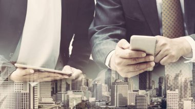 Cep telefonu ile modern şehir binaları arka plan kullanarak genç iş adamları. Gelecekteki telekomünikasyon teknolojisi ve internet şeyler (çok) kavramının.