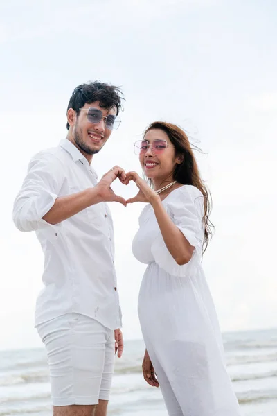 年轻夫妇在夏天在海滩显示心脏形状手手势 — 图库照片
