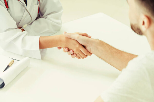 Woman doctor doing handshake with male patient in hospital office room. Healthcare and medical service occupation.