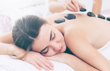 Kadın kaplıca salonunda profesyonel güzellik terapisti tarafından sıcak taş masajı görüyor. Lüks sağlık, sırt stresi ve gençleştirme kavramı..