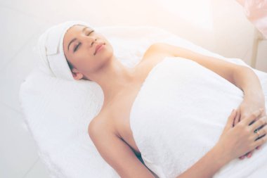 Spa yatağında uzanan rahat genç bir kadın lüks bir spa merkezinde yüz bakımı ve masaj için hazırlandı. Sağlık, stres atma ve gençleştirme kavramı.