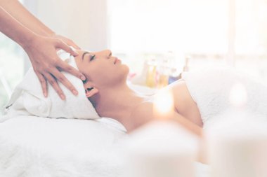 Lüks bir spa merkezinde masaj terapisti tarafından yüz masajı ve spa tedavisi için kaplıcaya uzanmış rahat bir kadın. Sağlık, stres atma ve gençleştirme kavramı.