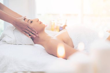 Lüks bir spa merkezinde masaj terapisti tarafından yüz masajı ve spa tedavisi için kaplıcaya uzanmış rahat bir kadın. Sağlık, stres atma ve gençleştirme kavramı.
