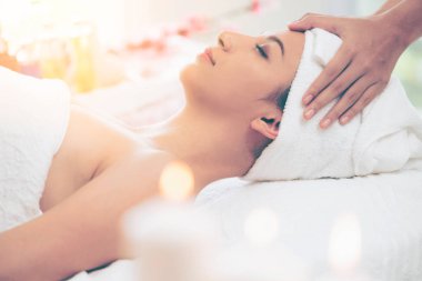 Lüks bir spa merkezinde masaj terapisti tarafından yüz masajı ve spa tedavisi için kaplıcaya uzanmış rahat bir kadın. Sağlık, stres atma ve gençleştirme kavramı.
