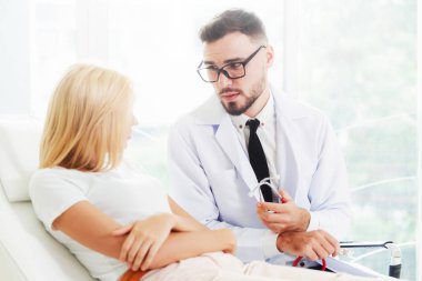 Erkek doktor konuşuyor ve Bayan hasta hastane ofisinde inceleyerek. Sağlık ve tıbbi hizmet.