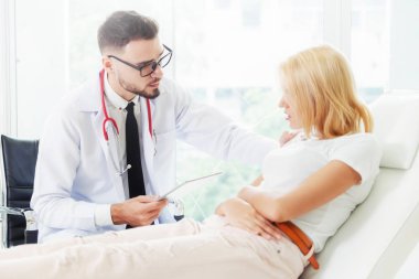 Erkek doktor konuşuyor ve Bayan hasta hastane ofisinde inceleyerek. Sağlık ve tıbbi hizmet.