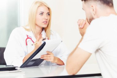 Kadın doktor konuşuyor ve erkek hasta hastane ofisinde inceleyerek. Sağlık ve tıbbi hizmet.