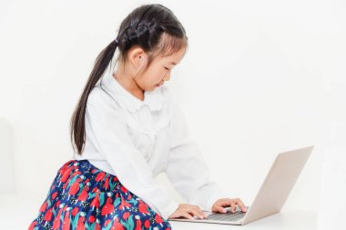 Beyaz koltukta oturan dizüstü bilgisayar kullanan küçük mutlu bir çocukluk. Çocukluk yaşam tarzı.