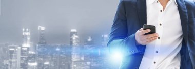 Genç işadamı cep telefonunuzun ve modern şehir binaları arka plan ile. Gelecekteki telekomünikasyon teknolojisi ve internet şeyler (çok) kavramının.