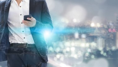 Genç işadamı cep telefonunuzun ve modern şehir binaları arka plan ile. Gelecekteki telekomünikasyon teknolojisi ve internet şeyler (çok) kavramının.