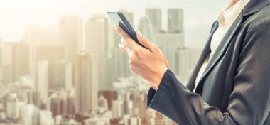 Cep telefonu ile modern şehir binaları arka plan kullanarak genç iş kadını. Gelecekteki telekomünikasyon teknolojisi ve internet şeyler (çok) kavramının.