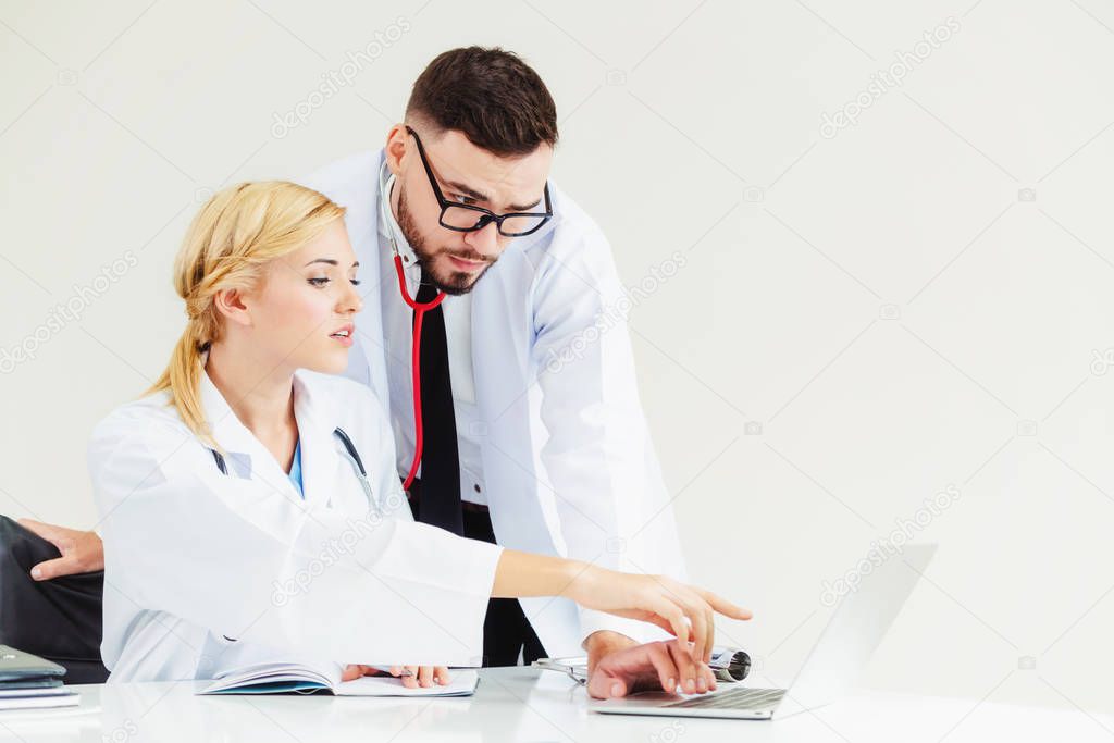 Doctor at hospital office working on laptop computer on the table with another doctor having discussion about patients health.