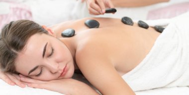 Kadın kaplıca salonunda profesyonel güzellik terapisti tarafından sıcak taş masajı görüyor. Lüks sağlık, sırt stresi ve gençleştirme kavramı..