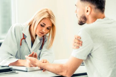 Kadın doktor konuşuyor ve erkek hasta hastane ofisinde inceleyerek. Sağlık ve tıbbi hizmet.