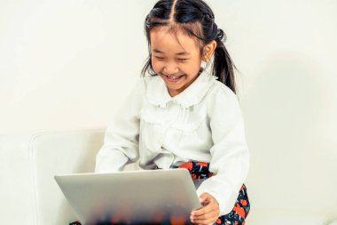 Beyaz koltukta oturan dizüstü bilgisayar kullanan küçük mutlu bir çocukluk. Çocukluk yaşam tarzı.