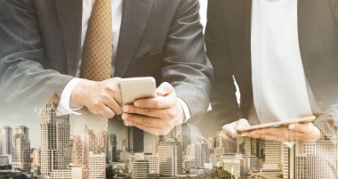 Cep telefonu ile modern şehir binaları arka plan kullanarak genç iş adamları. Gelecekteki telekomünikasyon teknolojisi ve internet şeyler (çok) kavramının.