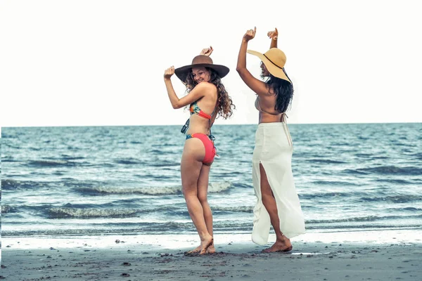 Happy women in bikinis dance together on tropical sand beach in summer vacation. Travel lifestyle.