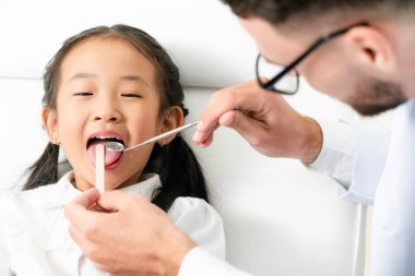 Mutlu çocuk diş diş kliniği içinde inceleyerek dostu genç diş hekimi. Diş Hekimliği kavramı.