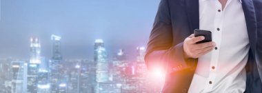 Genç işadamı cep telefonunuzun ve modern şehir binaları arka plan ile. Gelecekteki telekomünikasyon teknolojisi ve internet şeyler (çok) kavramının.