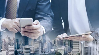 Cep telefonu ile modern şehir binaları arka plan kullanarak genç iş adamları. Gelecekteki telekomünikasyon teknolojisi ve internet şeyler (çok) kavramının.