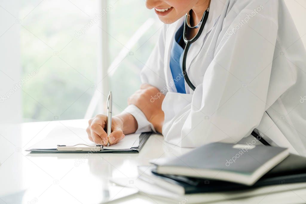 Woman doctor talks to female patient while writing on the patient health record in hospital office. Healthcare and medical service.