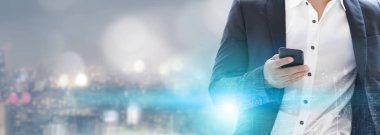 Genç işadamı cep telefonunuzun ve modern şehir binaları arka plan ile. Gelecekteki telekomünikasyon teknolojisi ve internet şeyler (çok) kavramının.