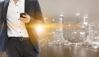 Genç işadamı cep telefonunuzun ve modern şehir binaları arka plan ile. Gelecekteki telekomünikasyon teknolojisi ve internet şeyler (çok) kavramının.