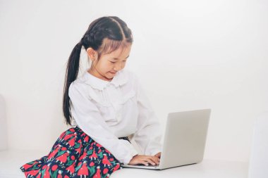 Beyaz koltukta oturan dizüstü bilgisayar kullanan küçük mutlu bir çocukluk. Çocukluk yaşam tarzı.