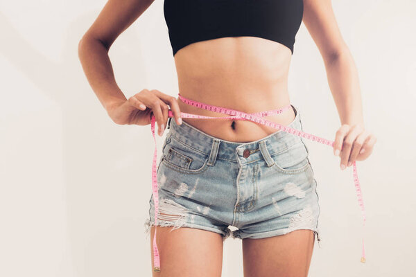 Young slim woman measures her waist by measuring tape after diet against white backgrounds. Concept of weight loss success.