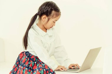 Beyaz koltukta oturan dizüstü bilgisayar kullanan küçük mutlu bir çocukluk. Çocukluk yaşam tarzı.