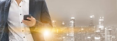 Genç işadamı cep telefonunuzun ve modern şehir binaları arka plan ile. Gelecekteki telekomünikasyon teknolojisi ve internet şeyler (çok) kavramının.