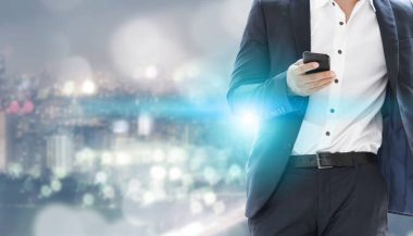Genç işadamı cep telefonunuzun ve modern şehir binaları arka plan ile. Gelecekteki telekomünikasyon teknolojisi ve internet şeyler (çok) kavramının.