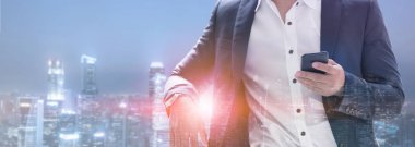 Genç işadamı cep telefonunuzun ve modern şehir binaları arka plan ile. Gelecekteki telekomünikasyon teknolojisi ve internet şeyler (çok) kavramının.