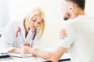 Kadın doktor konuşuyor ve erkek hasta hastane ofisinde inceleyerek. Sağlık ve tıbbi hizmet.
