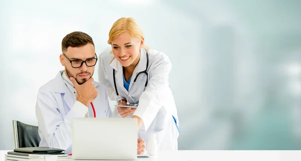 Doctor working with laptop computer at the office while having discussion with another doctor in the hospital. Medical healthcare and doctor service.