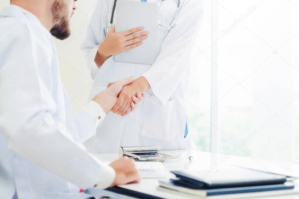 Doctor at the hospital giving handshake to another doctor showing success and teamwork of professional healthcare staff.