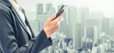 Cep telefonu ile modern şehir binaları arka plan kullanarak genç iş kadını. Gelecekteki telekomünikasyon teknolojisi ve internet şeyler (çok) kavramının.