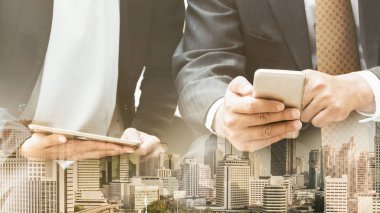 Cep telefonu ile modern şehir binaları arka plan kullanarak genç iş adamları. Gelecekteki telekomünikasyon teknolojisi ve internet şeyler (çok) kavramının.