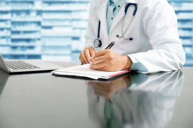 Erkek eczacı masada oturuyor ve eczane ofisindeki bir evrak raporunu yazıyor. Tıbbi sağlık personeli ve ilaç hizmetleri.